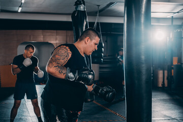 Male boxer training with punching bag in dark sports hall