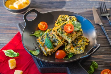 Sliced omelet or frittata with spinach and cheese on a black plate on a dark wooden background. Spinach recipes.