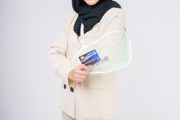 Portrait of young muslim woman with an injured arm in a sling over blue background in studio.