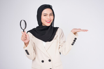 Young beautiful muslim woman in suit holding magnifying glass over white background studio