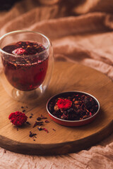 A glass cup of fragrant red tea on a wooden board next to scattered dry tea. Brew tea.