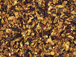 Red fruit tea with nut pieces and hibiscus leaves background. Aromatic tea made from fruits, spices and nuts. Dry pieces of apple, berries, spices and pieces of nuts close-up. Delicious drink.