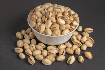 White bowl of pistachios on dark background