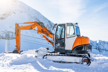 Small excavator on tops of snowy mountains, ski resort.