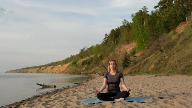 Adult woman on beach does yoga sitting in lotus position.