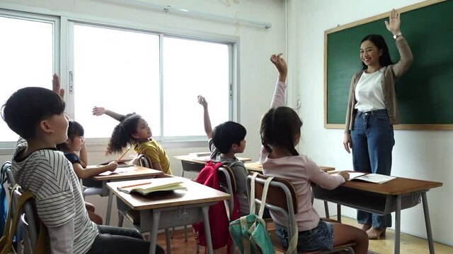Group of diverse elementary school kids with notebooks sitting in classroom and raise arm up to answer teacher question. Education, elementary school, learning, Back to school concept 