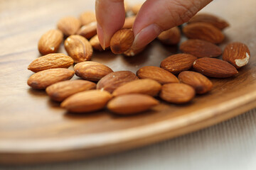 木の皿に乗ったアーモンドを指でつまむ