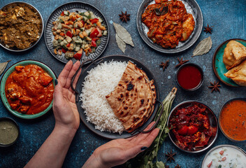 Assorted Indian ethnic food buffet on rustic concrete table from above: curry, fried samosa, rice...