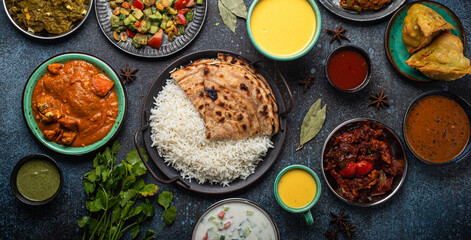 Assorted Indian ethnic food buffet on rustic concrete table from above: curry, fried samosa, rice...