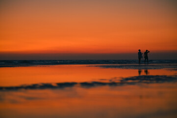 Fototapeta premium Summer sunset view on the beach. Beautiful blazing sunset landscape and orange sky above it with sun reflection on waves.