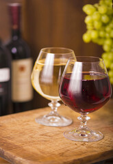 Two wine glass with white and red wine and grapes on wooden background.