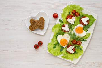 Breakfast on Valentine's Day. A plate of heart-shaped scrambled eggs, tomatoes, cheese and herbs and grain bread. View from above. Space for text. Diet breakfast.