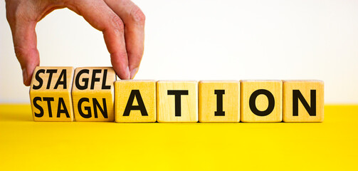 Stagflation or stagnation symbol. Businessman turns cubes, changes the word stagnation to stagflation. Beautiful yellow table white background, copy space. Business stagflation or stagnation concept.