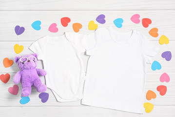 Mockup white child shirt and newborn onesie with paper colorful hearts and teddy bear in glass....