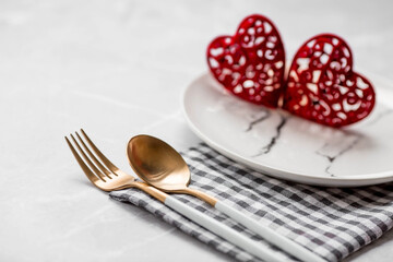 Banner. Table setting. A fashionable marble plate with a napkin, fork and red hearts on a gray background. Valentine's Day holiday concept for cafes and restaurants. A copy of the place for the text.