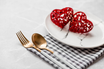 Banner. Table setting. A fashionable marble plate with a napkin, fork and red hearts on a gray background. Valentine's Day holiday concept for cafes and restaurants. A copy of the place for the text.