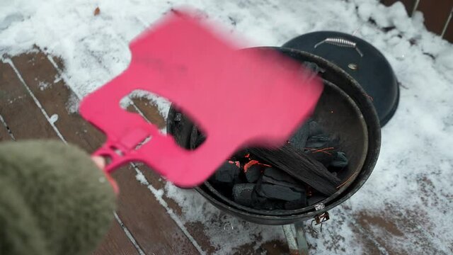 Burning fire in a round small barbecue. In the courtyard of the house, in winter. top view.Man is circumcised. Blows up the fire.