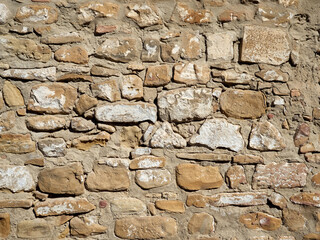Close up of a brown whitewashed wall made with uneven stones and cement. Beige background