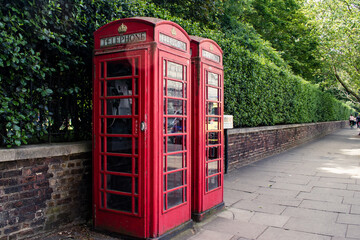 Red London telephone booths in front of stone wall and green bushes