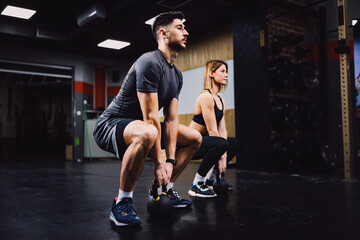 A fitness couple doing powerlift exercises with kettlebells in a gym.