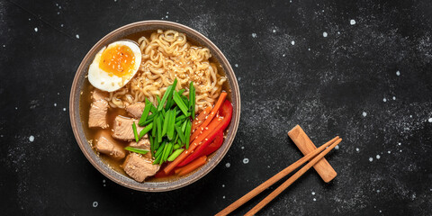 Ramen noodle soup with chicken, vegetables and eggs. Black rustic stone background. Top view. Japanese food. Banner