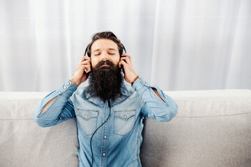 Relaxed bearded man listening music while sitting on the sofa at home.