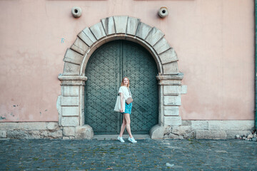 Fototapeta na wymiar Happy blonde woman posing in the front having fun on background of old wooden door at european street in Lviv, Ukraine