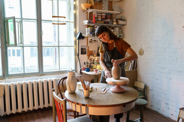 Creative woman art classes student or workshop owner creating potter vase in studio. Female...