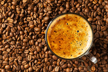 a cup of coffee with foam on the background of coffee beans top view