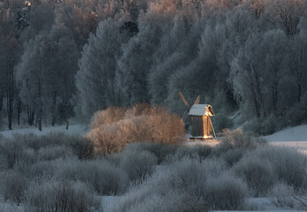 Winter beautiful fairy tale. An old wooden mill in a field under the snow near the river soaring in...