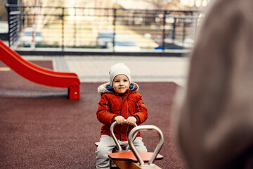 A little boy on the seesaw at the playground with mother of father.