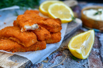 Close up of   Crispy breaded  deep fried fish fingers with breadcrumbs served  with remoulade sauce and  lemon Cod Fish Nuggets on rustic wood table background