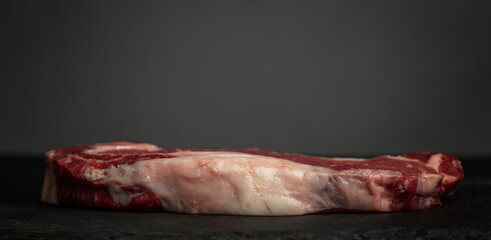 Raw marbled beef ribeye steak. Side view, profile. Big plan. Black background. Space for text. Panorama format.