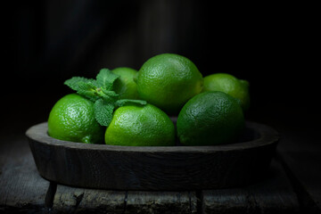 Still life with fresh lime in a wooden dish on a wooden background.