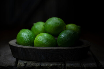 Still life with fresh lime in a wooden dish on a wooden background.
