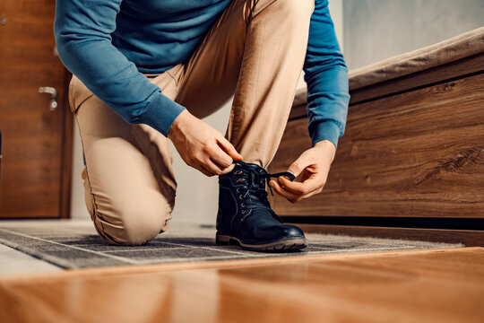 A man in shoes or boots. A man is kneeling at home, tying his shoelace, and preparing to go outside.