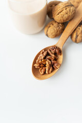 Vegan milk from nuts in a glass cup with various nuts on a white table, nuts in a wooden spoon.