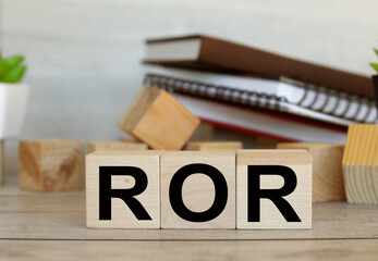 ROR text on wooden cubes. wood blocks are stacked in two rows. in the background notepad and plants