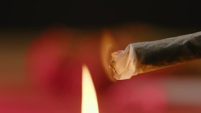 Flame lighting up a rolled marijuana joint on a background with blinking, red and blue lights, close-up shot.