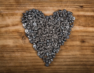 A heart shaped figure laid out from screws on vintage brown wooden board. Concept of metallic artificial heart machine, robot, mechanism, Valentine Day, strong eternal love. Free text space.