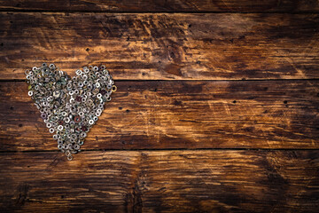A heart shaped figure laid out from screws on vintage brown wooden board. Concept of metallic...