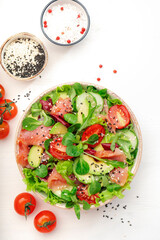 Spring salad with salted salmon, avocado, tomatoes, cucumber, black sesame seeds, olive oil, and mixed herbs. White background, top view, copy space