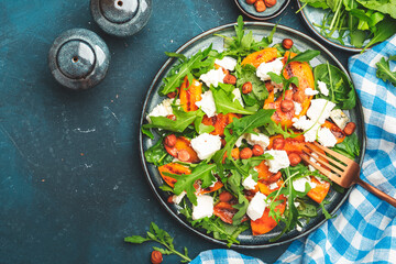 Summer salad with grilled peach with soft cheese, hazelnuts and arugula on blue table background, top view, copy space