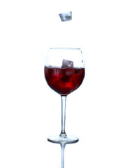 Red soda in a wine glass with ice cubes on the white background. Ice cubes are falling from above to the wine glass. One of them is frozen in the flight.