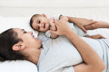 Happy mother lying on bed with her little baby - Family and Maternity concept