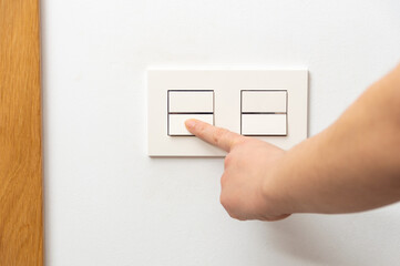 Close up of female finger is turn on or off on light switch with white wall at home copy space.