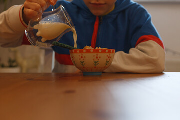 A boy pouring milk into a bowl of cereal - obrazy, fototapety, plakaty