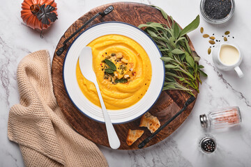 Pumpkin traditional soup with creamy silky texture with sage leaves and red pepper in white plate or bowl. Light grey background. Copy space. Mock up. Top view, flat lay.