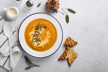 Pumpkin traditional soup with creamy silky texture with sage leaves and red pepper in white plate or bowl. Light grey background. Copy space. Mock up. Top view, flat lay.