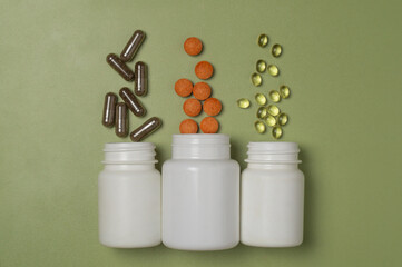 Multi-colored pills and capsules with vitamins or dietary supplements fly out of three white plastic jars